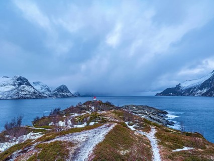 Small lighthouse at the end of Husøy island with a view across the fjord to the sea, Senja island,