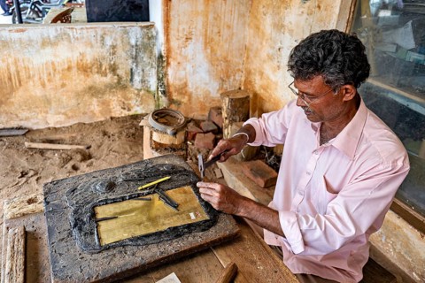 Man doing traditional crafts with tools on metal plate in rustic workshop, A craftsman working in