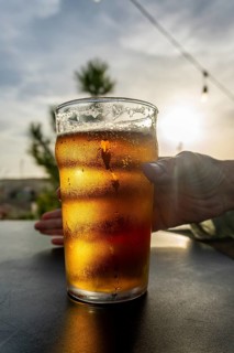 Hand holding condensation covered pint of cold beer on a table at sunset, golden light and foamy