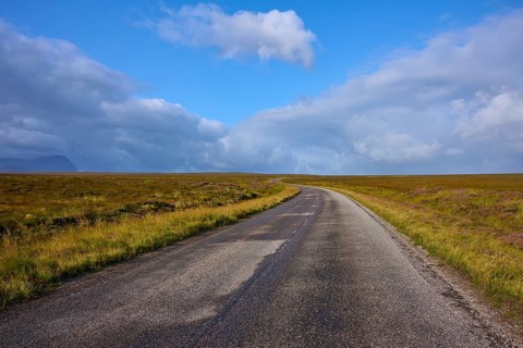 A deserted paved road stretches through an open landscape against a cloudy sky, Tongue, Lairg,