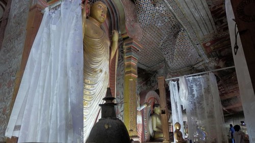 Cave room with large Buddha statue, artfully painted walls and curtains, Dambulla cave temple, Sri