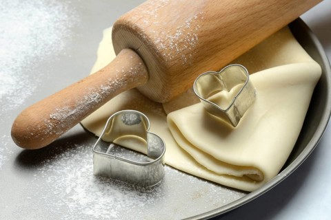 Rolled dough on cake tray with dough rollers and cookie cutters