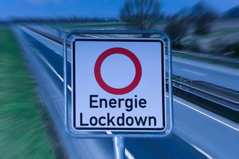 (photo montage) Road sign with text ENERGY LOCKDOWN in front of an empty highway
