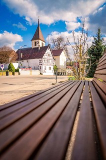 Wooden bench in a quiet suburb, with half-timbered church and houses in the background under cloudy