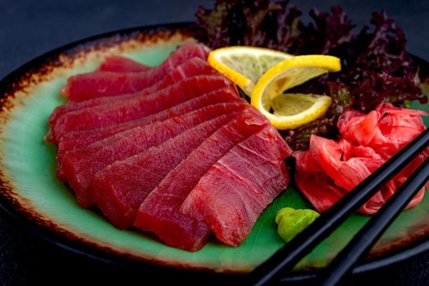 Fresh tuna sashimi served with lemon, wasabi, and pickled ginger on a dark background