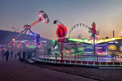 Lively fair with illuminated rides in motion at dusk, carousel and the hustle and bustle of summer