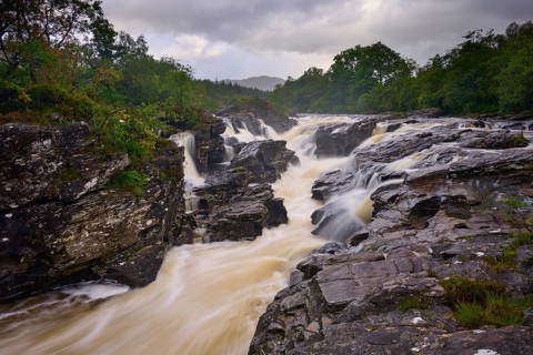 A wild river with turbulent flows and rock formations, surrounded by natural scenery, River Orchy,