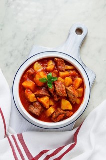Potatoes stewed with meat, in tomato sauce, with spices and herbs, no people, on a white table