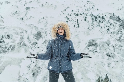A joyful person stands in falling snow, clad in a winter jacket and gloves, at Astun ski resort in