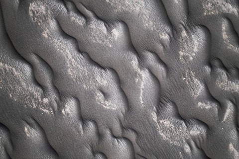 Close-up image capturing the intricate patterns formed on a black sand beach, showcasing textures