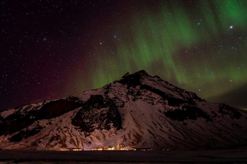 A breathtaking view of the Northern Lights dancing over a snow-covered mountain in Iceland. The