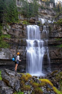 Young pretty hiker standing on rocks in front of Cascata di Mezzo waterfall, long exposure,
