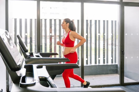 A pregnant woman in a red outfit exercises on a treadmill, promoting fitness and wellness during