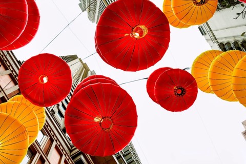 From below vibrant red and yellow lanterns hanging between buildings in Hong Kong during the