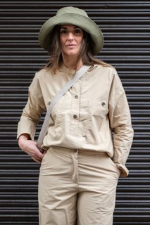 A woman stands confidently in a stylish safari outfit featuring khaki pants and a wide brimmed hat.