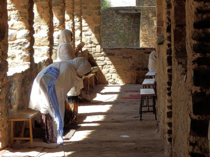 People pray in a shady area of stone corridor architecture, Debre Birhan Selassie Church, Fasil