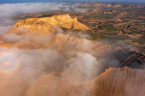A stunning aerial view of rugged desert cliffs partially shrouded in mist, juxtaposed with lush