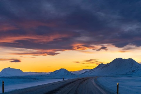 A serene winter drive through Iceland's snowy landscape at dusk. The vibrant sunset colors the sky,