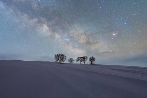 A serene nightscape in Iceland showcasing a starry sky above snow-covered hills and silhouetted