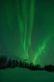 Vibrant green aurora borealis illuminates the night sky over a snow-covered landscape, with a
