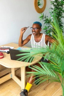 LGBTQIA+ man excitedly planning a holiday trip on a laptop. Surrounded by a cozy setting with