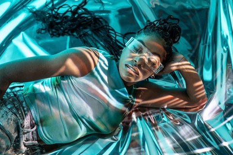 A futuristic African young woman lies in a reflective space, embodying the metaverse's immersive