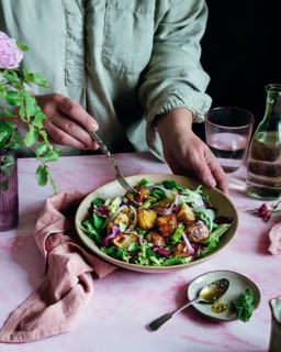 A person in a light shirt prepares a vibrant potato salad with fresh greens, roasted potatoes, and