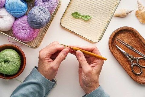 Top view cropped unrecognizable hands of a woman crocheting in her studio. Surrounded by colorful
