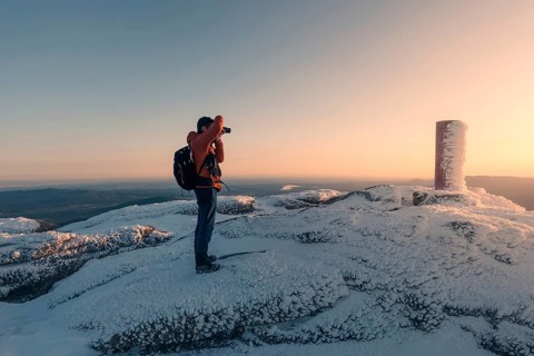 A photographer stands on the snowy summit of Siete Picos, capturing the serene sunrise over the