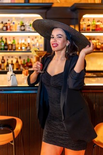 Vertical portrait of a chic woman with elegant hat drinking luxury cocktail