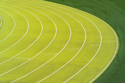 Overhead view of vibrant green lanes vividly marking the curves on an outdoor athletics stadium,