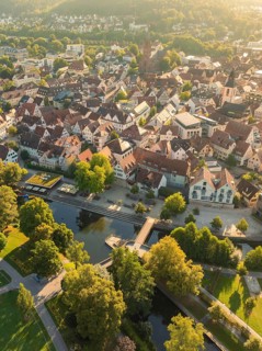 Town view with many houses and red roofs, a river with bridge and many trees at sunset, Nagold,
