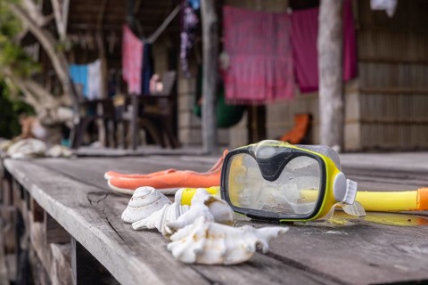 Snorkeling gear with seashells are laid out on a rustic wooden table on Kri Island, with blurred
