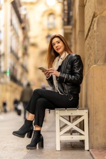 Stylish businesswoman browsing her smartphone while taking a break on a bench in a bustling city