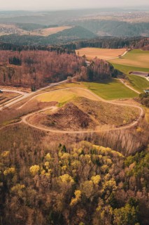 Wide view of a hilly landscape with forests and fields, bordered by a winding path, old deposit in