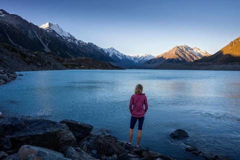 A woman is standing on the shores of Tasman Lake. On the left, Mount Cook. Golden hour. Aoraki