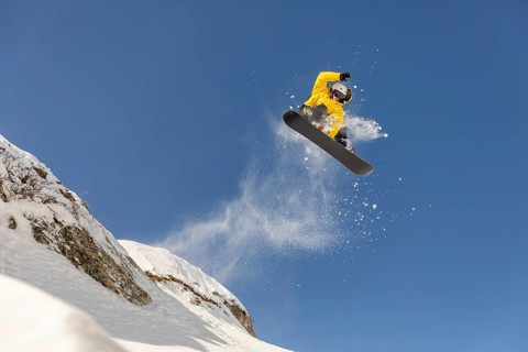 A snowboarder in a yellow jacket performs a thrilling jump in the backcountry, showcasing a