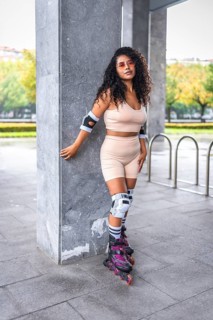 Portrait of a latin female skater with inline skates on a urban park standing leaning on column