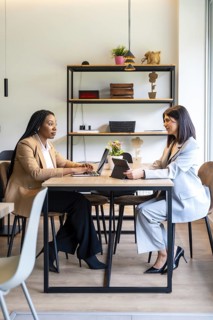 Two businesswomen are working together on their laptops and tablets in a hotel lobby, discussing