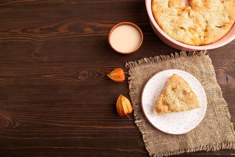 Apple Charlotte cake on brown wooden background and linen textile, cup of milk, top view, flat lay,