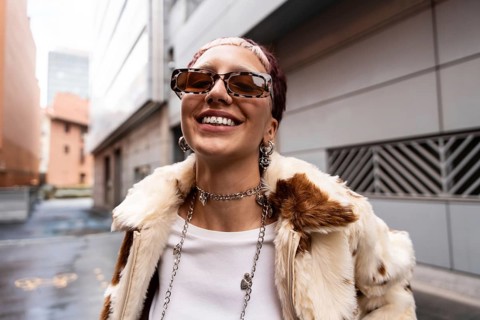 A fashionable woman with sunglasses smiles with tooth gem confidently looking at camera while