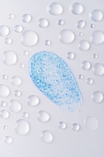 Close-up of face scrub smears with blue micro-exfoliating particles, surrounded by water droplets