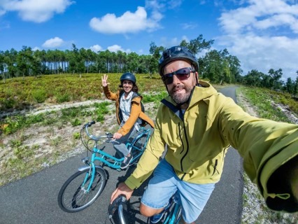 Happy couple cycling along a sunny pine lined path, taking a selfie together during an active
