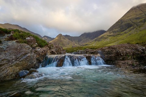 Small waterfall in a mountainous landscape under cloudy sky with clear water streams, Fairy Pools,