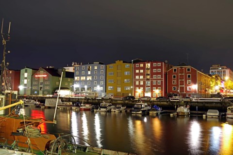 Colourful, illuminated buildings and boats on a quiet, reflected harbor at night, Nidelva,