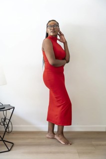 Businesswoman in a red dress is standing in her hotel room, touching her hair and looking away