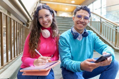 A cheerful young Gen Z woman with headphones and a tablet, and a man with headphones holding a