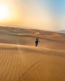 Smiling happy woman running in the vast Wahiba Sands Desert at sunrise, capturing the serene beauty