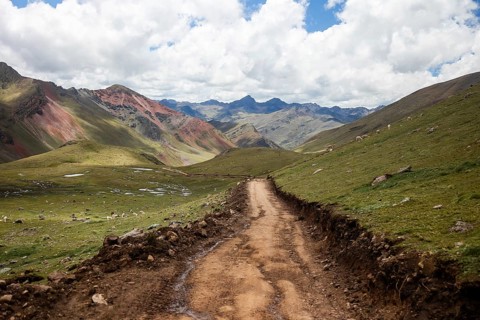 A scenic dirt trail meanders through the vibrant, multicolored Andean mountain scape, dotted with