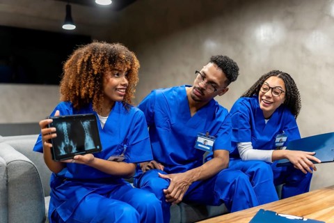 Healthcare students in blue scrubs collaborating on a medical case, reviewing a spinal x ray on a